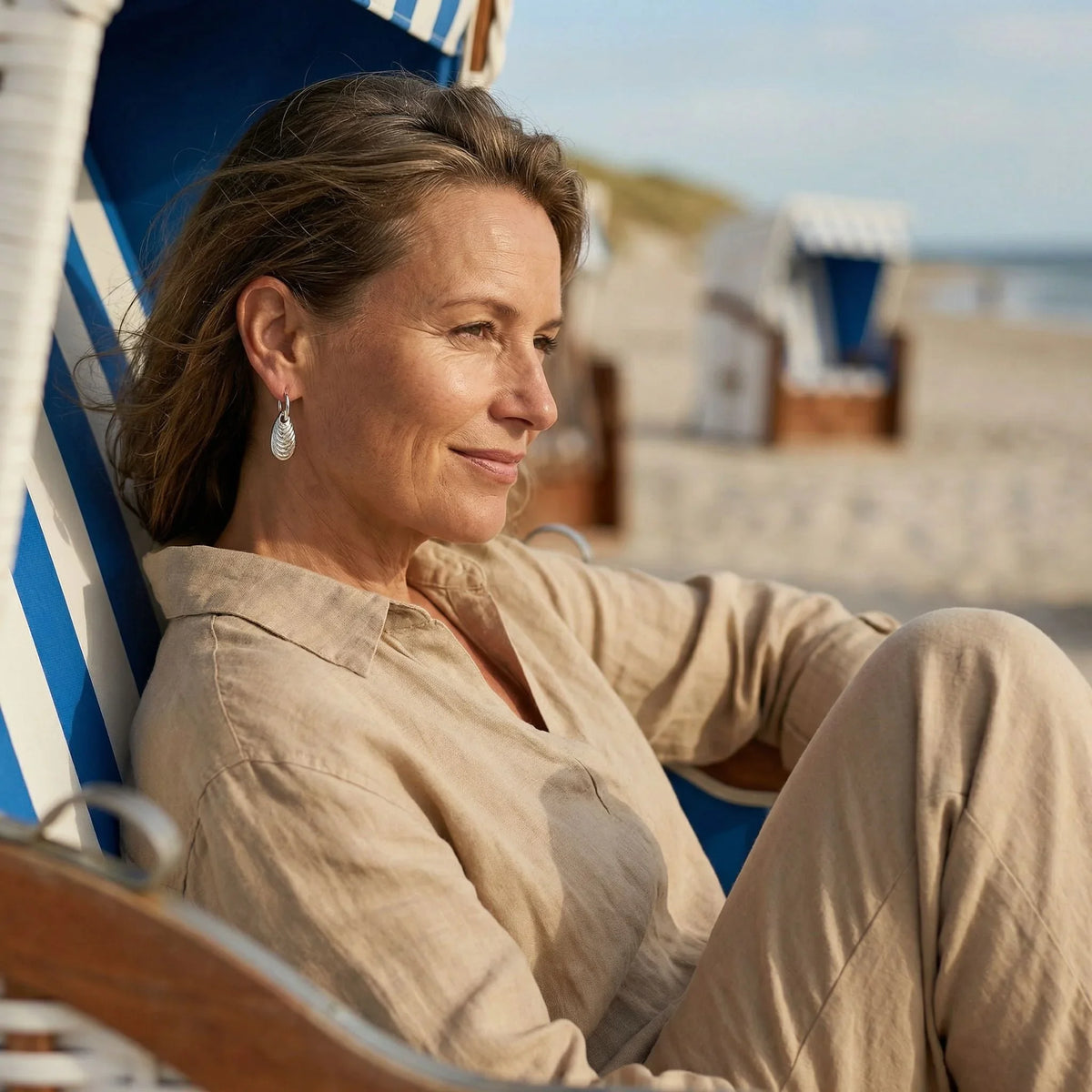 Frau am Strand im Strandkorb mit silbernem Miesmuschel-Anhänger-Ohrring, maritimer Schmuck