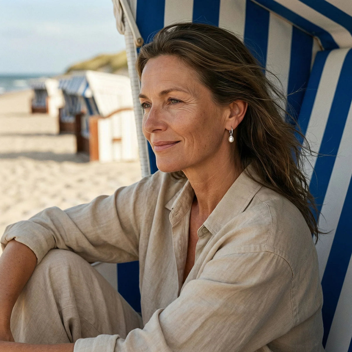 Frau am Strand trägt silberne Creolen mit Perle, maritimer Schmuck, entspannte Atmosphäre