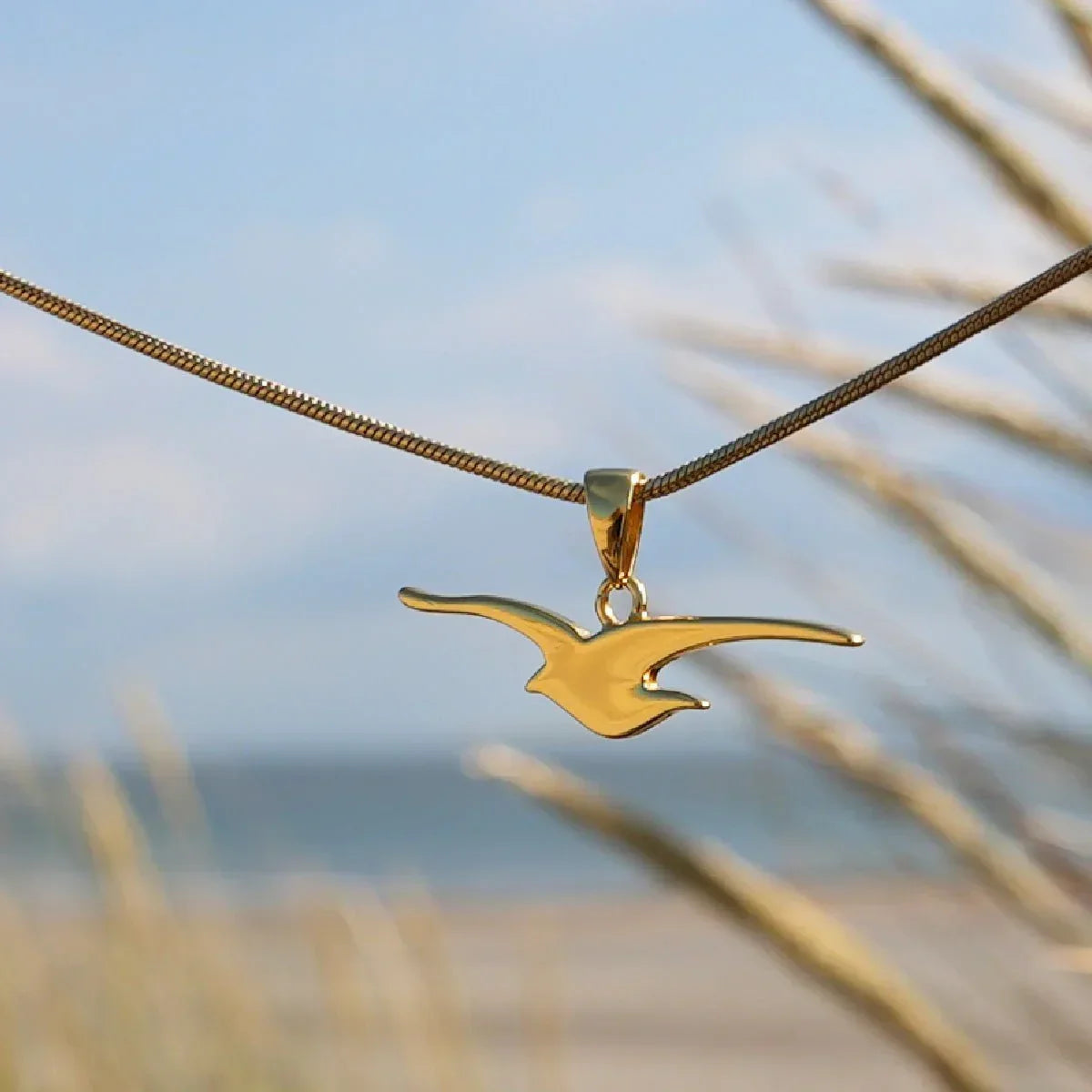 Goldene Möwe Anhänger Kette vor maritimer Strandkulisse, maritimer Schmuck