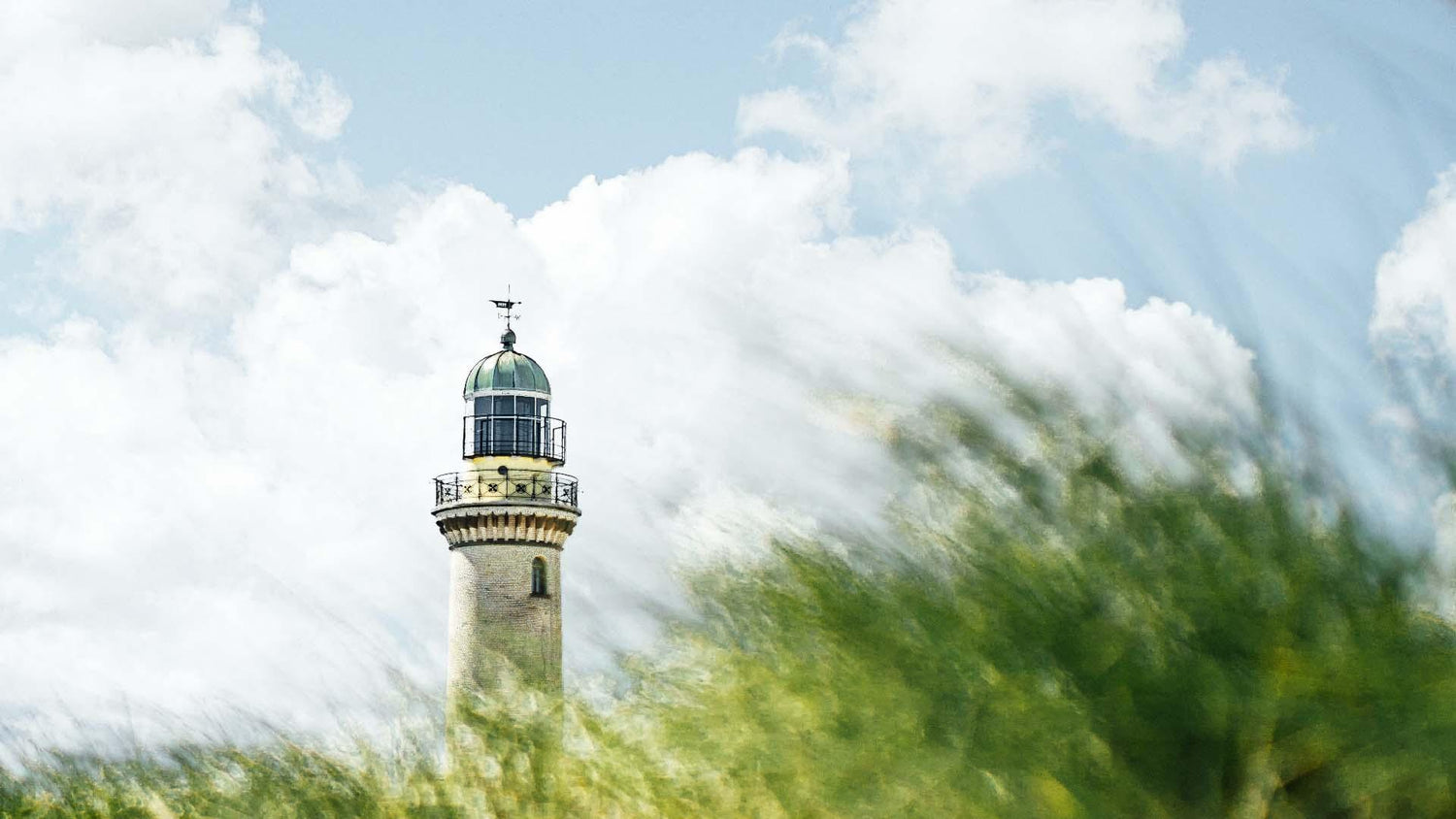 Leuchtturm an der Nordsee hinter Dünengras unter wolkigem Himmel, maritimes Küstenmotiv