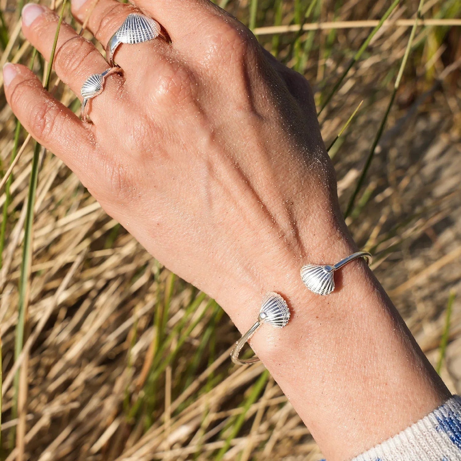 Silbernes Muschel-Armband und Ringe am Handgelenk, maritimer Schmuck am Strand