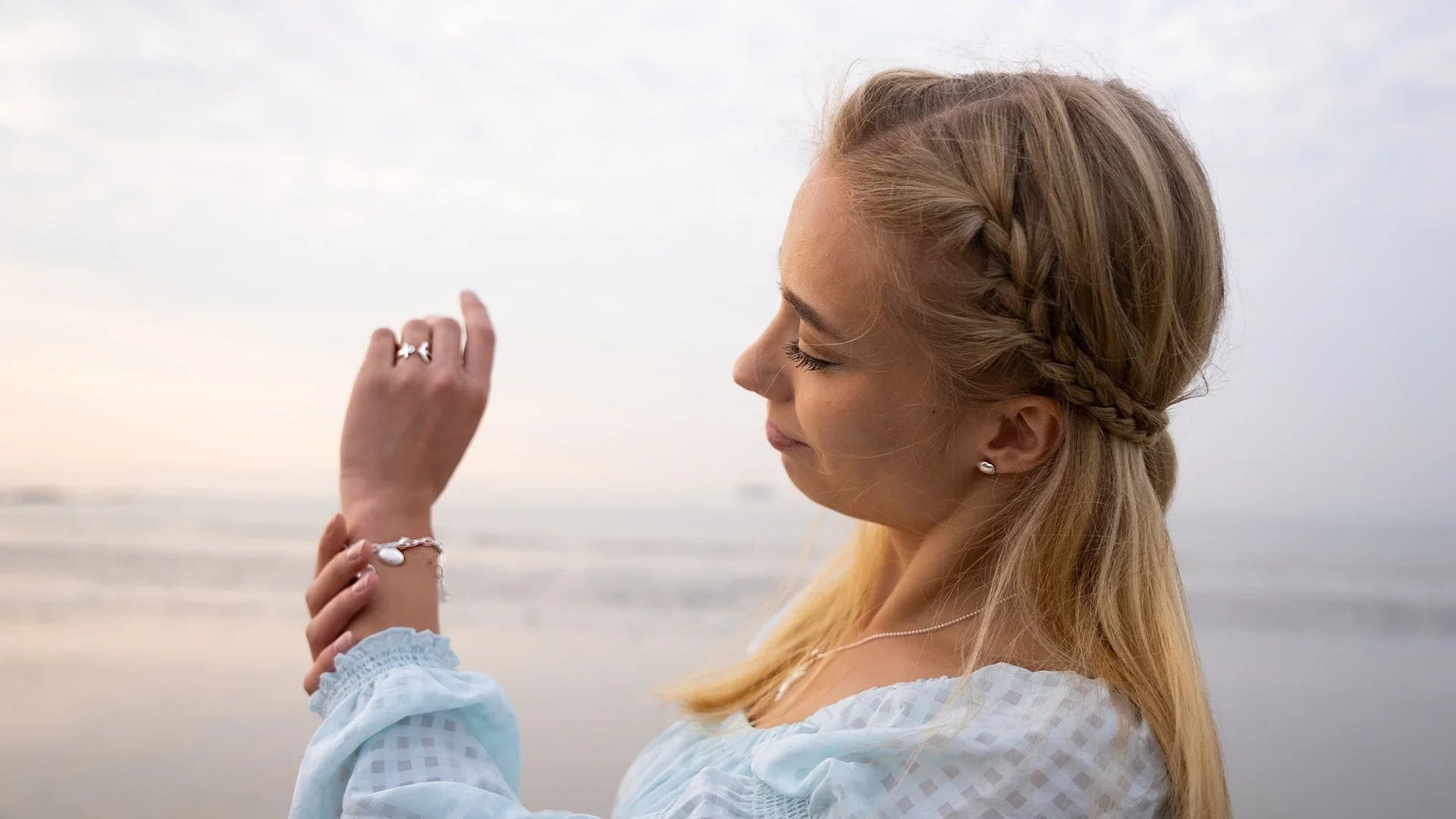 Frau am Strand mit maritimem Muschel-Armband und geflochtenem Haar, schmuck am Handgelenk