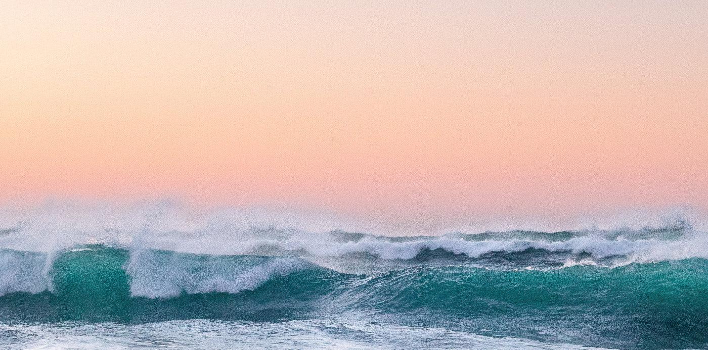 Wellen am Meer bei Sonnenuntergang, sanfter rosa Himmel, Küstenlandschaft