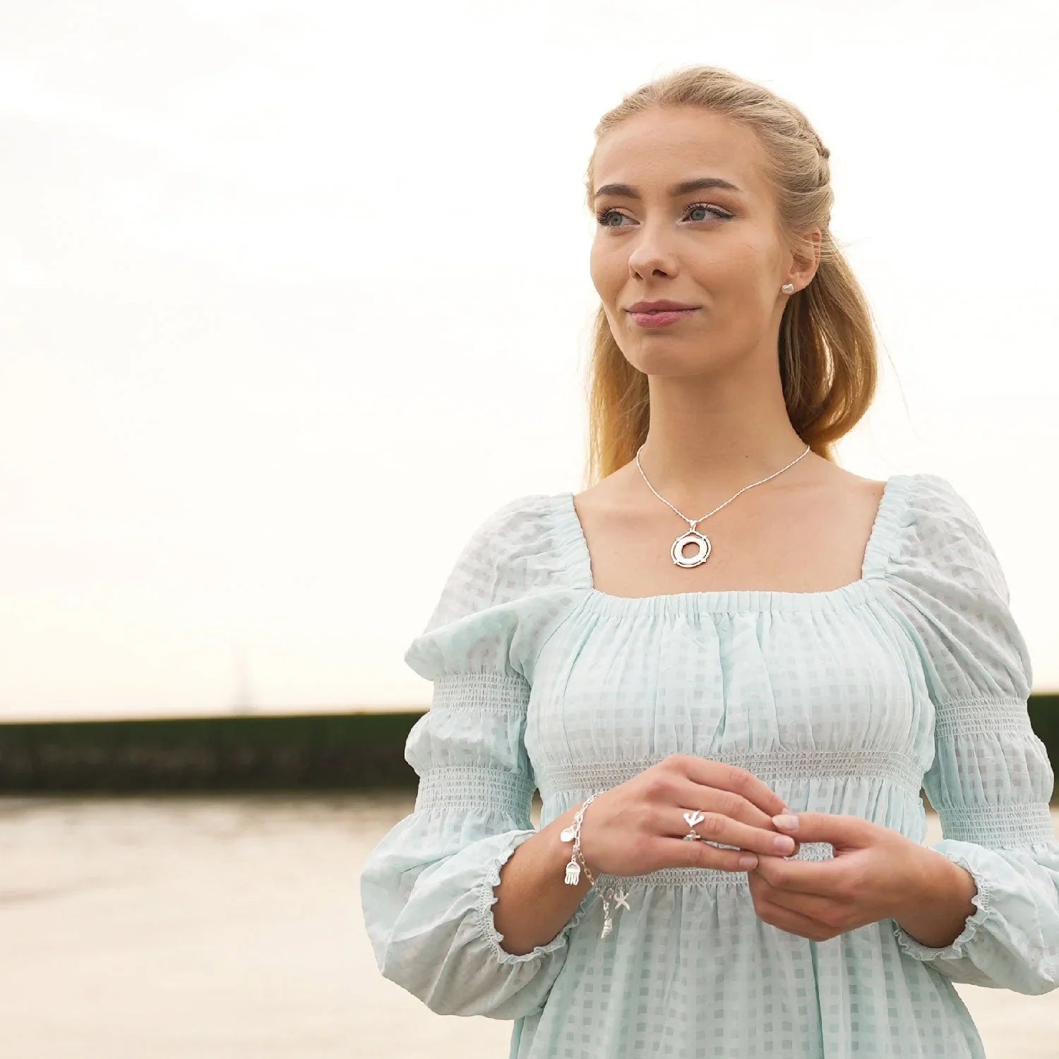 Frau mit maritimem Schmuck, Kette und Armband am Strand mit Küstenhintergrund