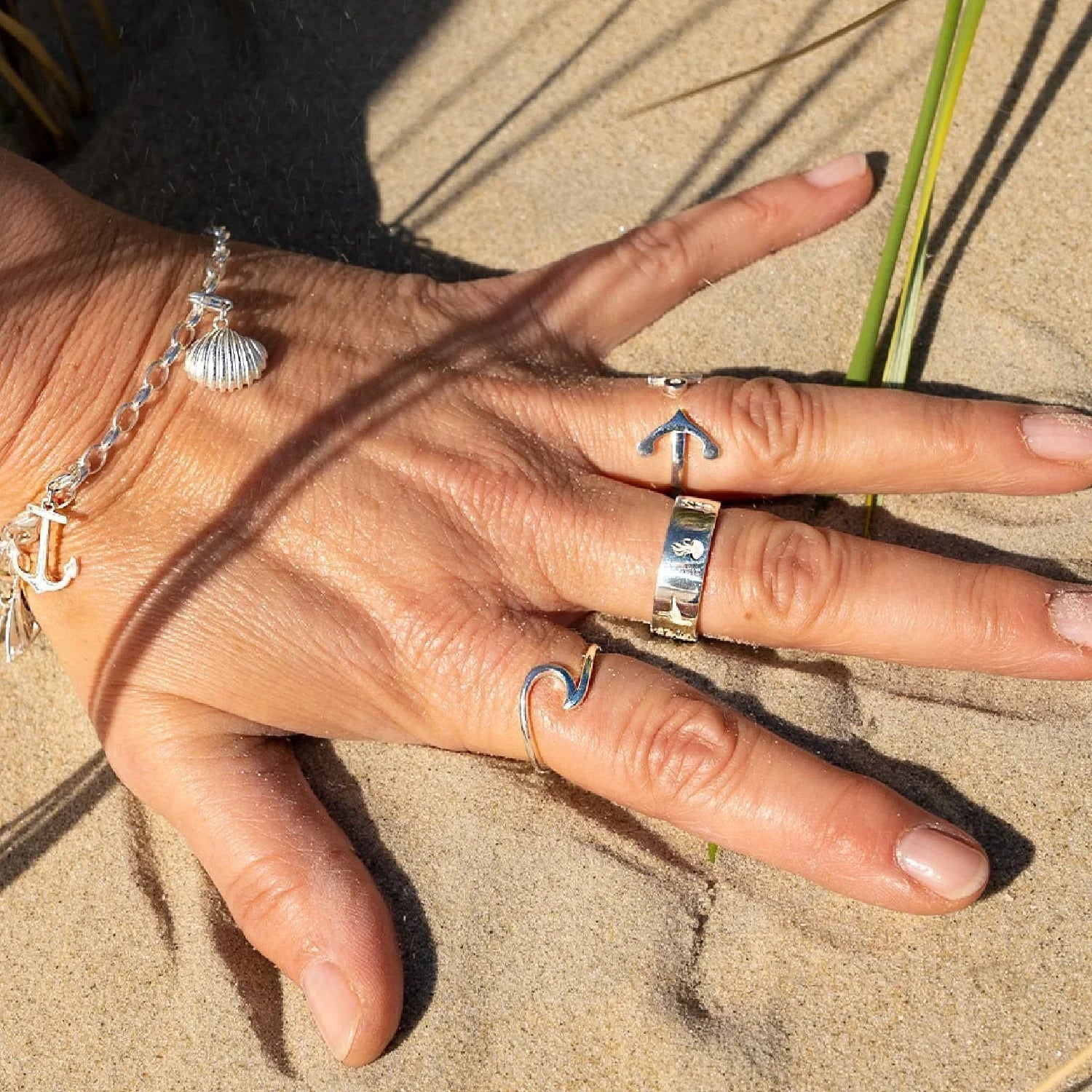 Silberne maritime Ringe und Armband mit Muschel auf Hand im Sand am Strand