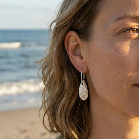 Silberner Miesmuschel-Ohrring am Ohr einer Frau am Strand, maritimer Schmuck