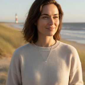 Frau mit silbernem Anhänger in Knotenform am Strand, Leuchtturm im Hintergrund