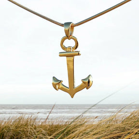 Goldener Anker-Anhänger an Kette vor Strand und Meer, maritimer Schmuck