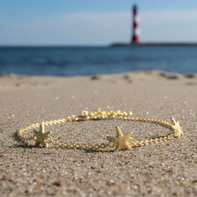 Goldenes Armband mit Seestern-Anhängern am Strand, maritimer Schmuck, Meer im Hintergrund