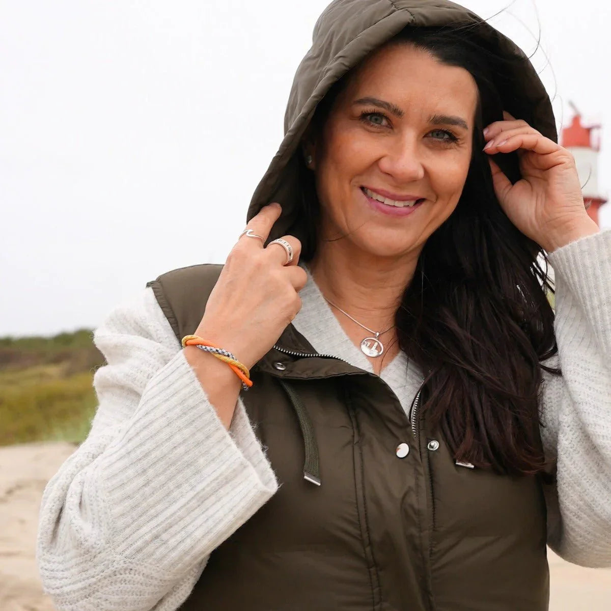 Frau am Strand mit maritimem Armband in orange und silber, Leuchtturm im Hintergrund