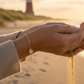 Goldenes Armband mit Knoten-Anhänger am Handgelenk am Strand bei Sonnenuntergang
