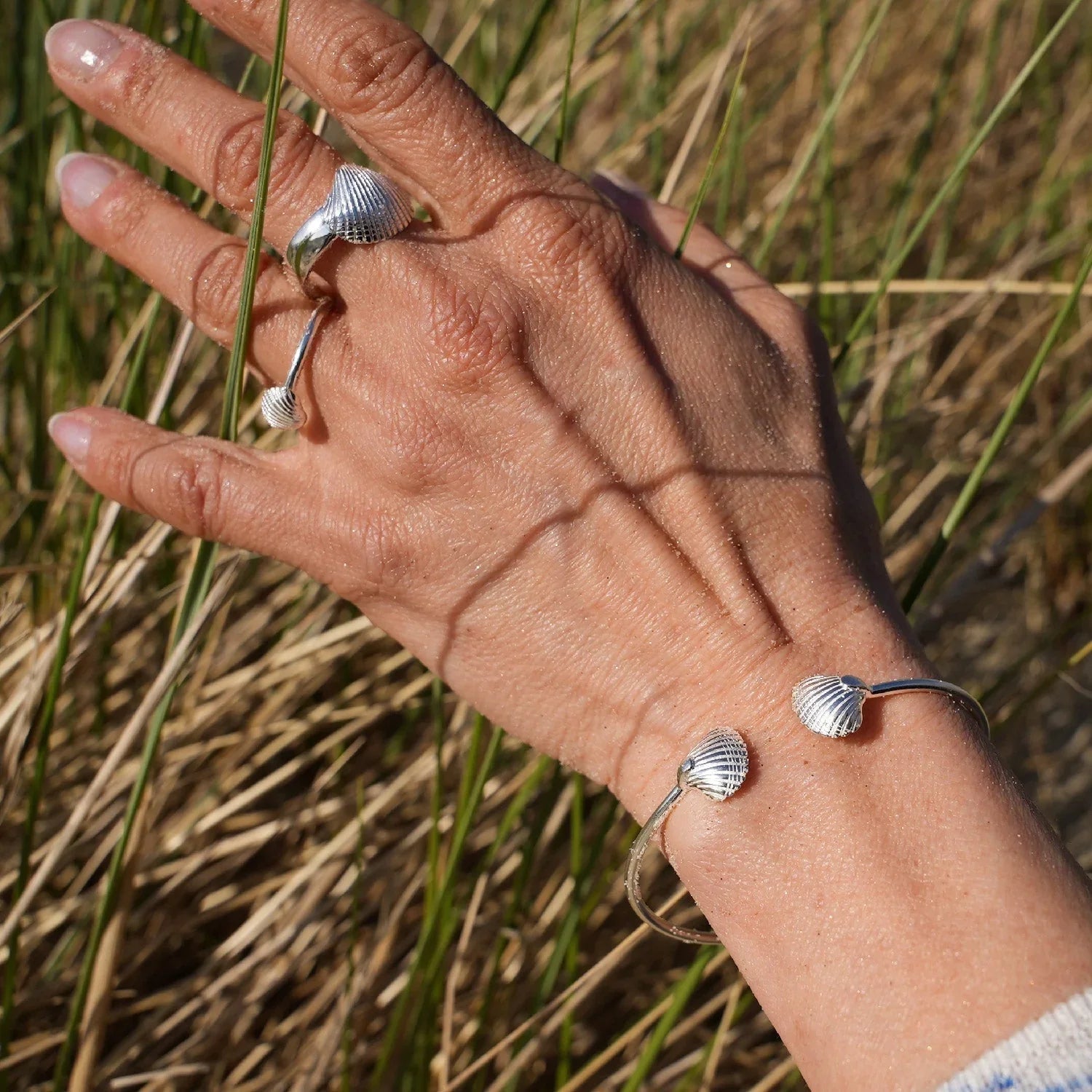 Silberner Armreif und Ring mit Muschel-Design getragen, maritimer Schmuck im Sonnenlicht