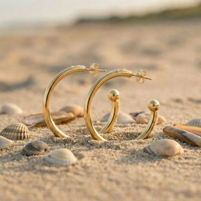 Goldene Creolen Ohrringe am Sandstrand mit Muscheln, maritimer Schmuck