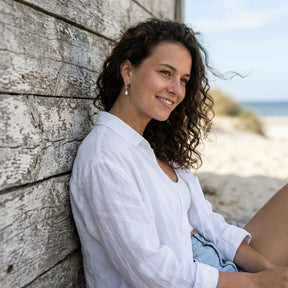 Frau am Strand mit silbernen Creolen-Ohrringen und Perlenanhänger, sommerlich gekleidet