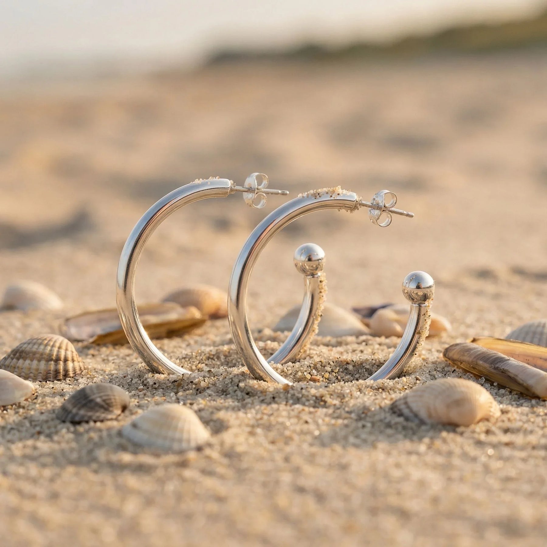 Silberne Creolen-Ohrringe für Anhänger im Sand mit Muscheln am Strand