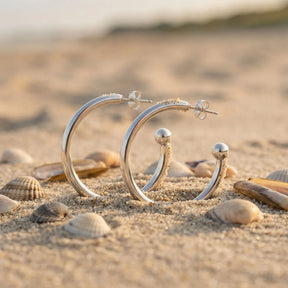 Silberne Creolen-Ohrringe für Anhänger im Sand mit Muscheln am Strand