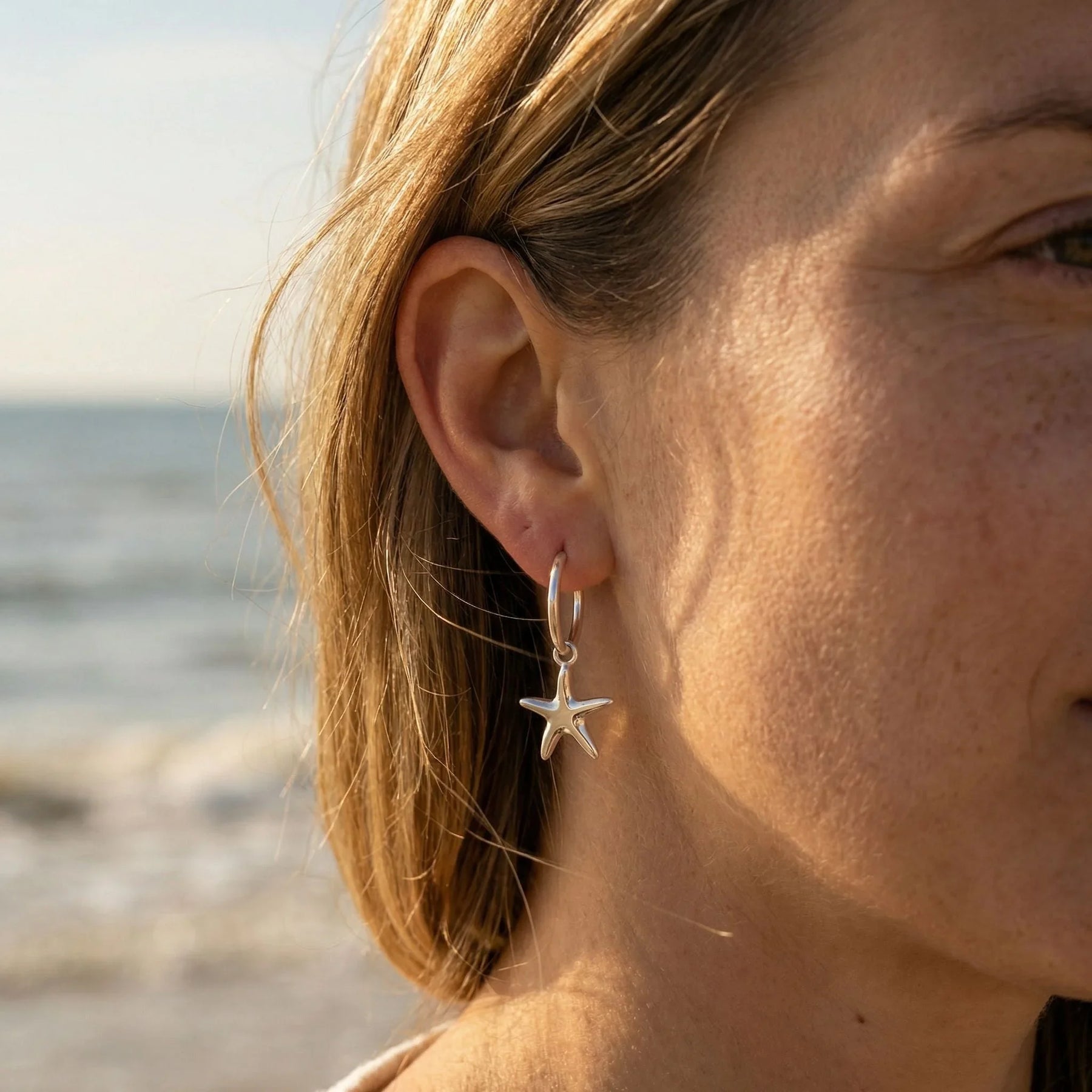 Silberne Creole mit Seestern-Anhänger am Ohr, maritimer Schmuck am Strand