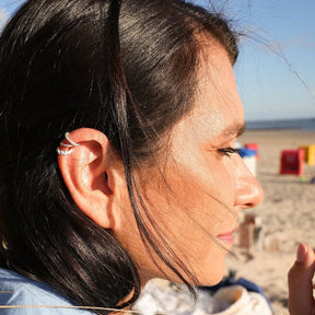 Silberner Muschel-Ohrring Ear Cuff am Ohr einer Frau am Strand, maritimer Schmuck