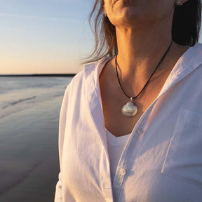 Frau am Strand mit Herzmuschel-Anhänger aus Silber an schwarzem Band, maritime Schmuckkette