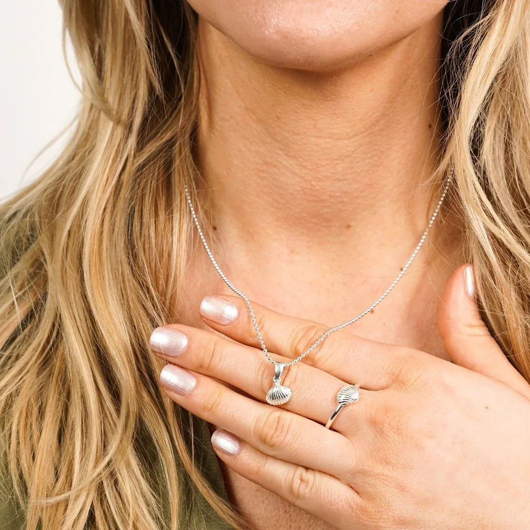 Silberne Halskette und Ring mit Herzmuschel-Anhänger, maritimer Schmuck am Dekolleté einer Frau