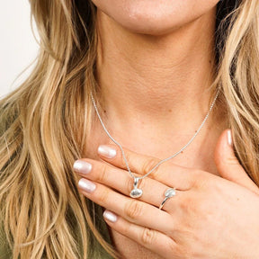 Silberne Halskette und Ring mit Herzmuschel-Anhänger, maritimer Schmuck am Dekolleté einer Frau