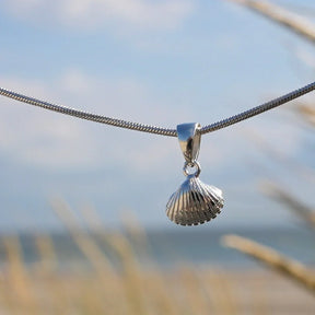 Silberner Herzmuschel Anhänger an Kette, maritimer Schmuck vor Strand und Meer