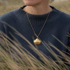Frau mit goldener Herzmuschel-Kette im maritimen Stil vor Dünenlandschaft