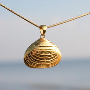 Goldene Klaffmuschel-Anhänger Kette maritimer Schmuck am Strand mit Meer im Hintergrund