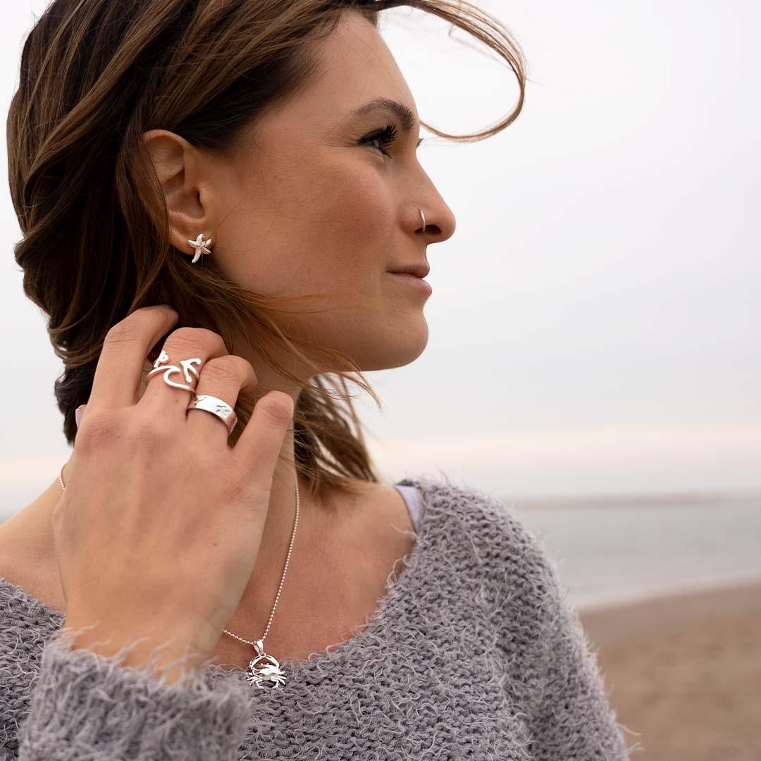 Frau am Strand mit maritimem Silberschmuck: Krebs-Anhänger, Seestern-Ohrring, Anker-Ring
