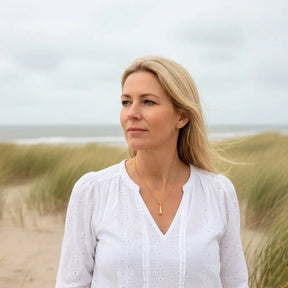 Frau mit goldener Leuchtturm-Kette am Strand vor Dünen und Meer, maritimer Schmuck