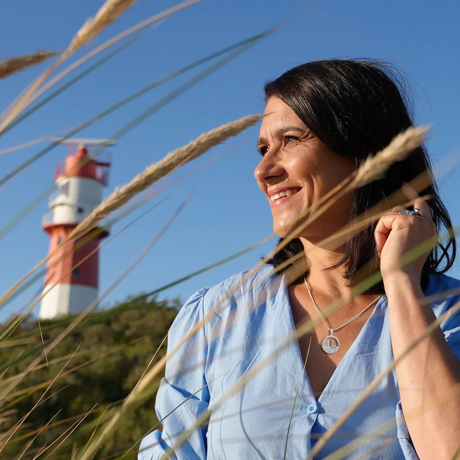 Frau mit silberner Leuchtturm-Kette im Dünen-Gras, maritimer Schmuck, Leuchtturm im Hintergrund
