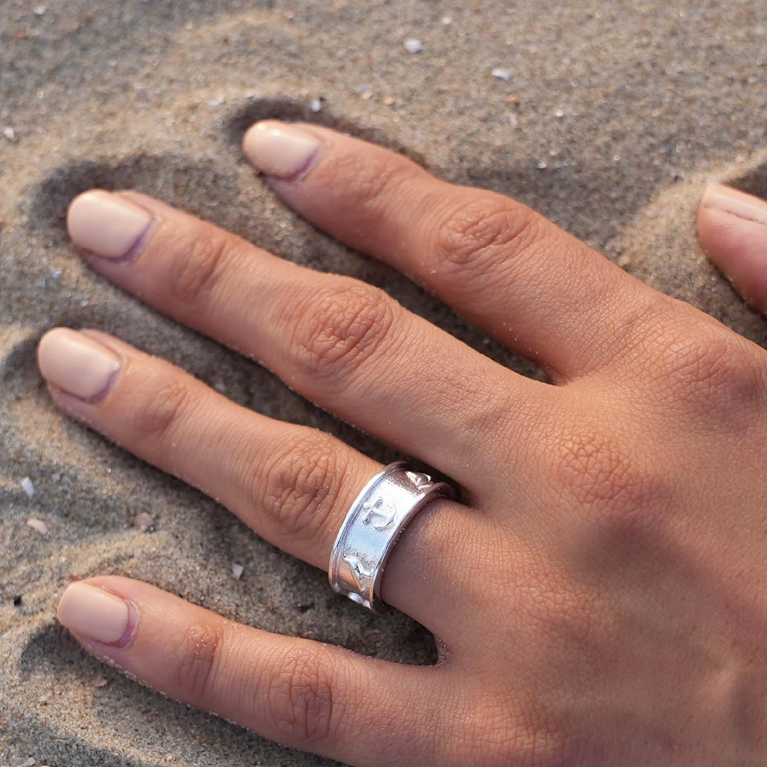 Silberner maritimer Ring mit Anker-Motiv am Finger auf Sand, Küsten-Schmuck