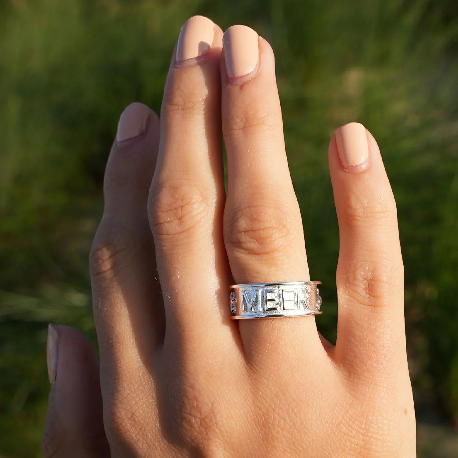 Silberner Ring mit Gravur 'MEER' am Finger, maritimer Schmuck, Nahaufnahme, Naturhintergrund