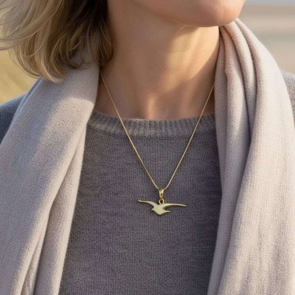 Frau trägt goldene Kette mit Möwen-Anhänger, maritimer Schmuck am Strand