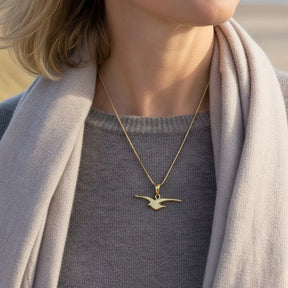 Frau trägt goldene Kette mit Möwen-Anhänger, maritimer Schmuck am Strand