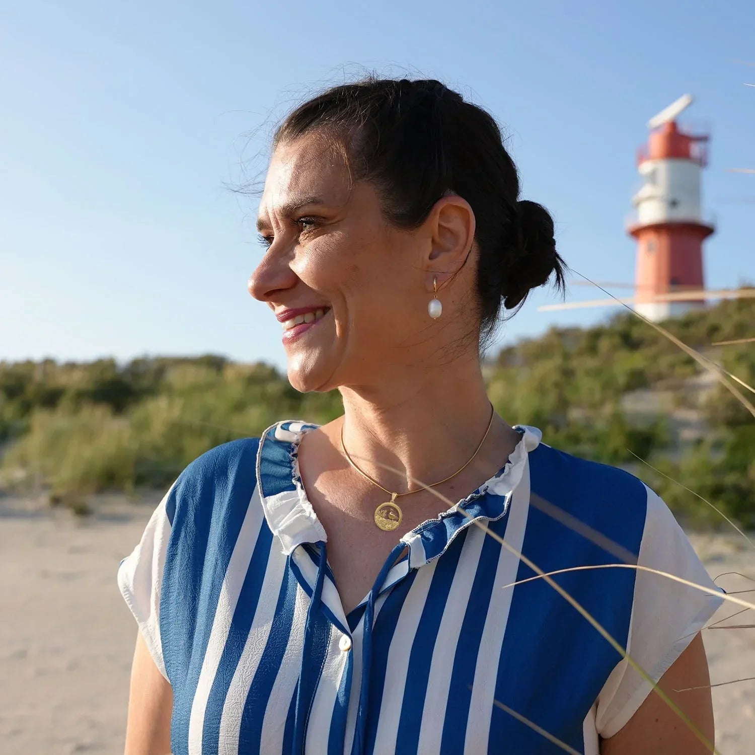 Frau mit goldener Möwenkette am Strand vor Leuchtturm, maritime Schmuckmode