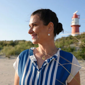 Frau mit goldener Möwenkette am Strand vor Leuchtturm, maritime Schmuckmode