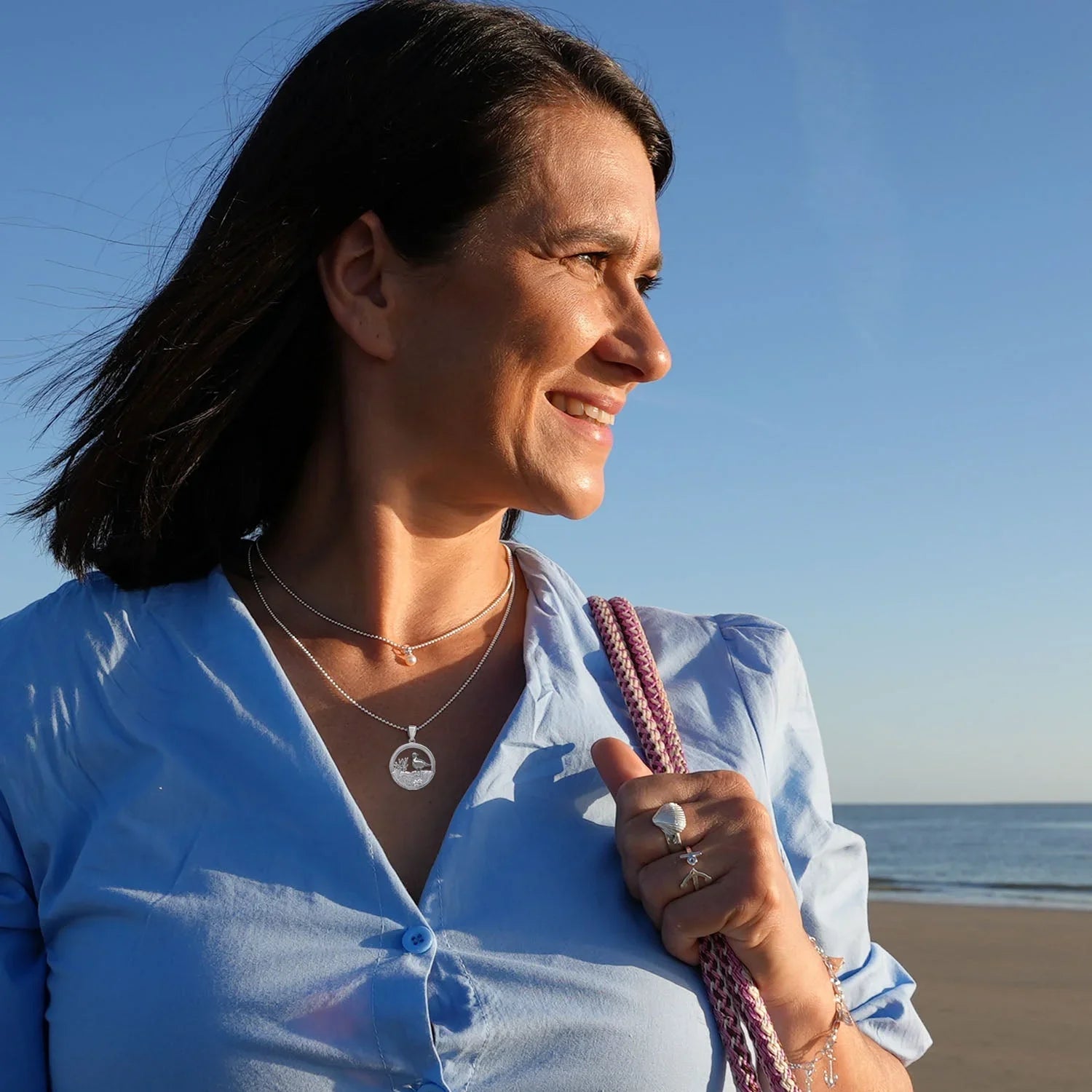Frau am Strand mit maritimer Silberkette und Schmuck, heller Himmel, Meereskulisse