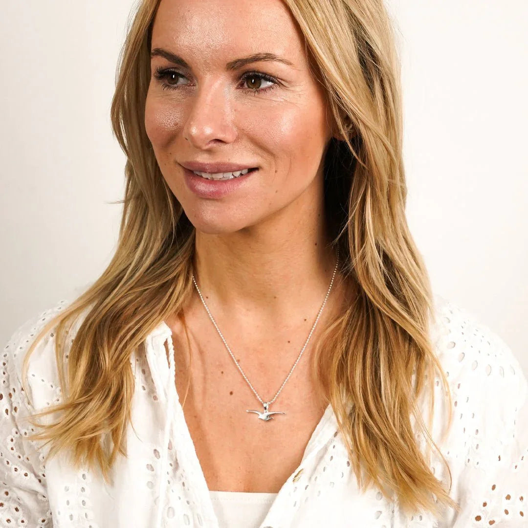 Frau mit maritimer Silberkette, Möwen-Anhänger, weißes Oberteil, Schmuck am Hals
