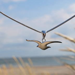 Silberkette mit Möwen-Anhänger vor maritimer Strandkulisse, maritimer Schmuck