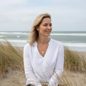 Frau am Strand trägt goldene Muschel-Halskette mit Perle, maritimer Schmuck, Küste im Hintergrund