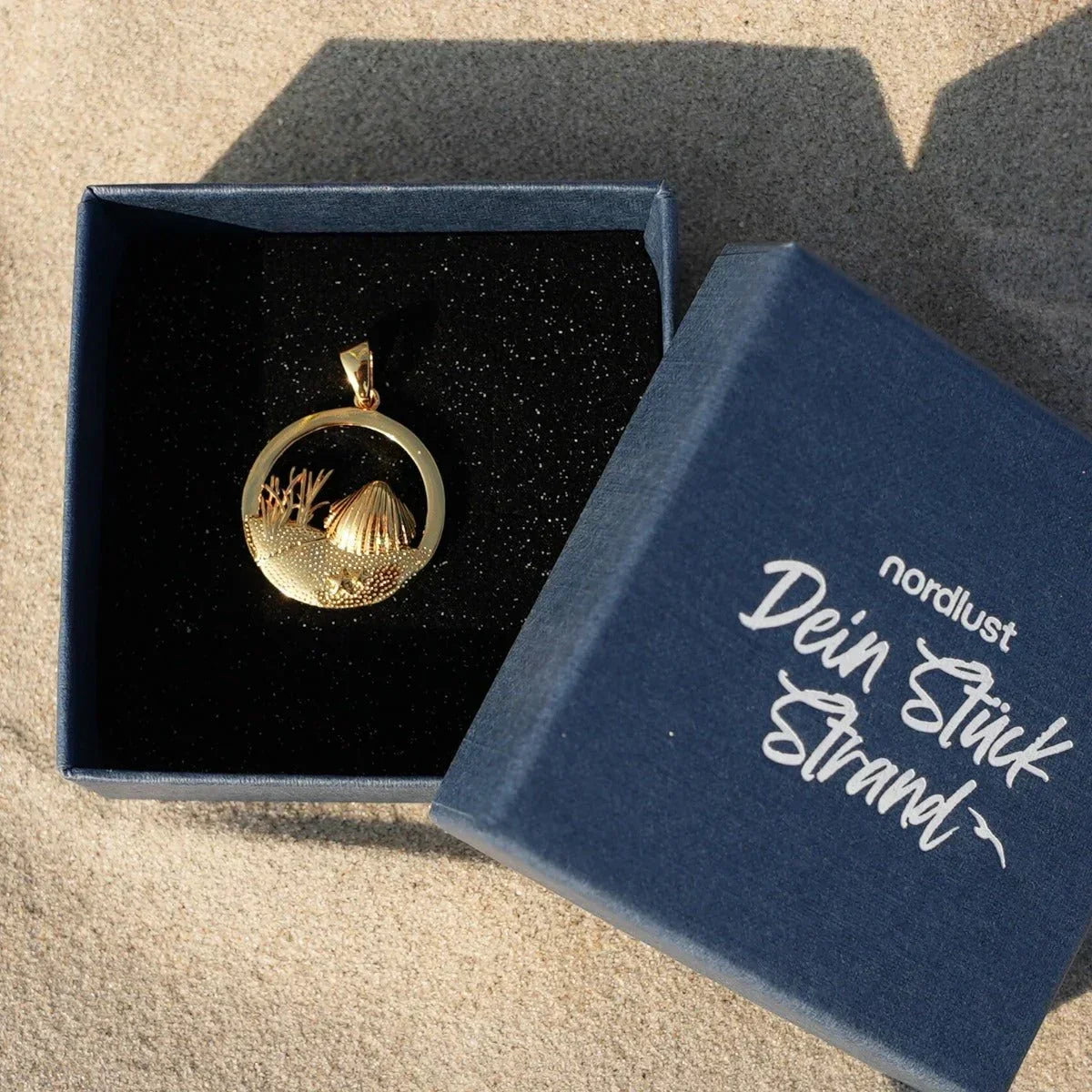 Goldener Muschel-Anhänger mit Dünenmotiv in Geschenkbox auf Sand, maritimer Schmuck