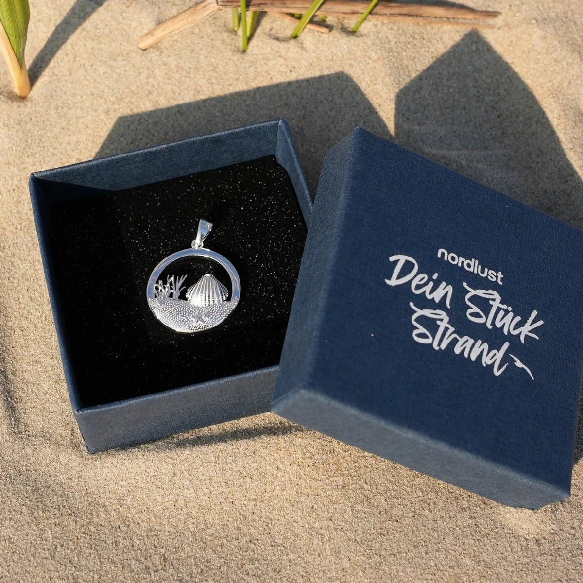 Silberner Anhänger Muschel rund mit Dünenmotiv in Schmuckschachtel auf Sand