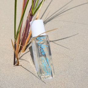 Eau de Parfum Flakon Wave mit weißem Deckel am Sandstrand neben Grashalmen, maritim