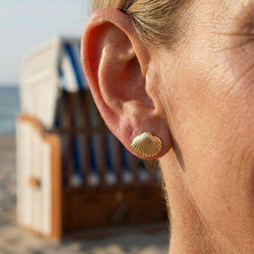Goldener Muschel-Ohrstecker am Ohr, maritimer Schmuck am Strand