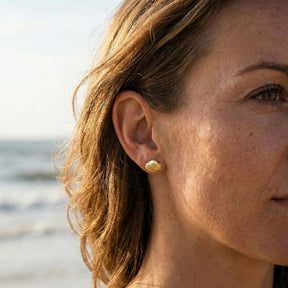 Goldene Herzmuschel Ohrstecker am Ohr einer Frau am Strand, maritimer Schmuck