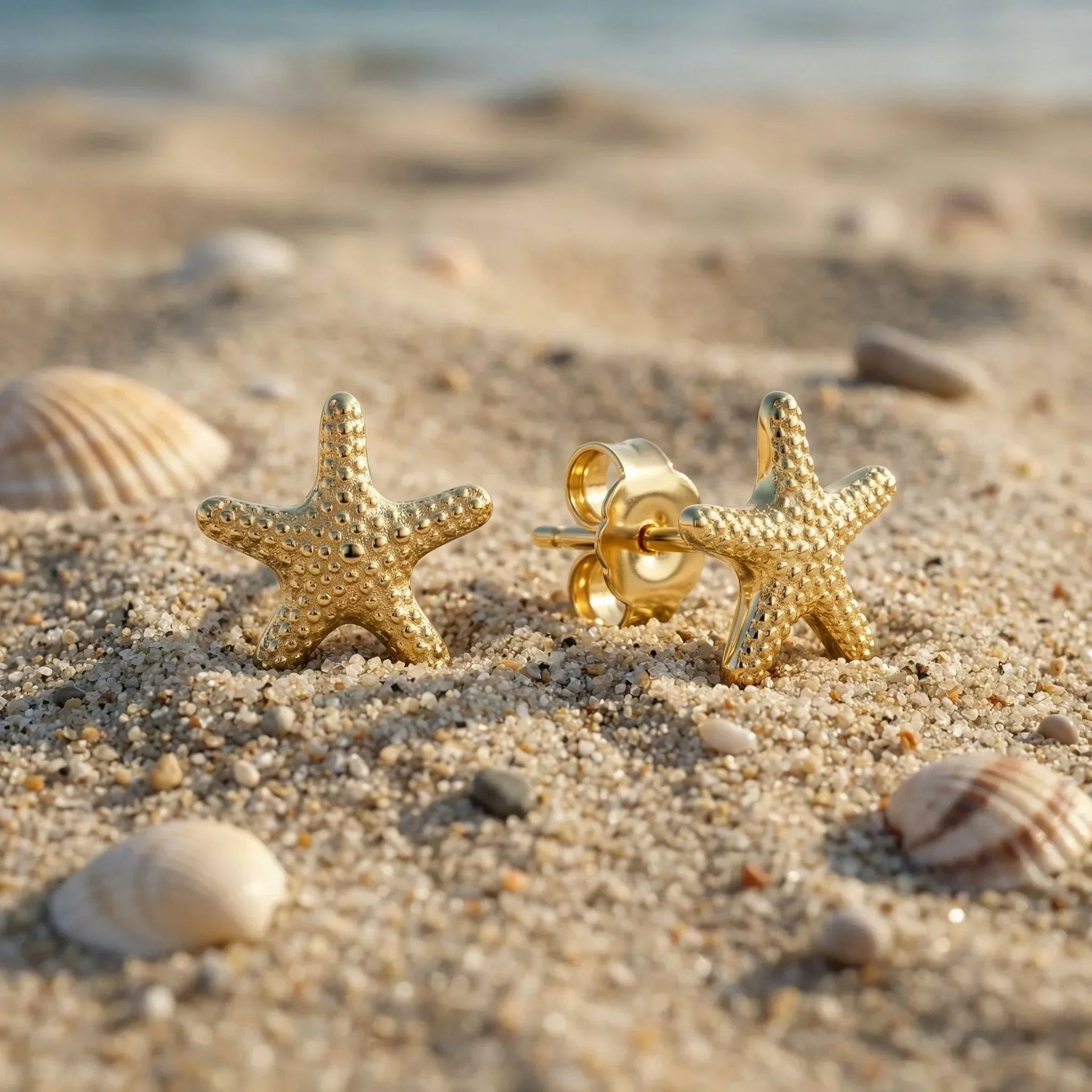 Goldene Seestern Ohrstecker auf Sand mit Muscheln am Strand, maritimer Schmuck