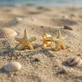 Goldene Seestern Ohrstecker auf Sand mit Muscheln am Strand, maritimer Schmuck