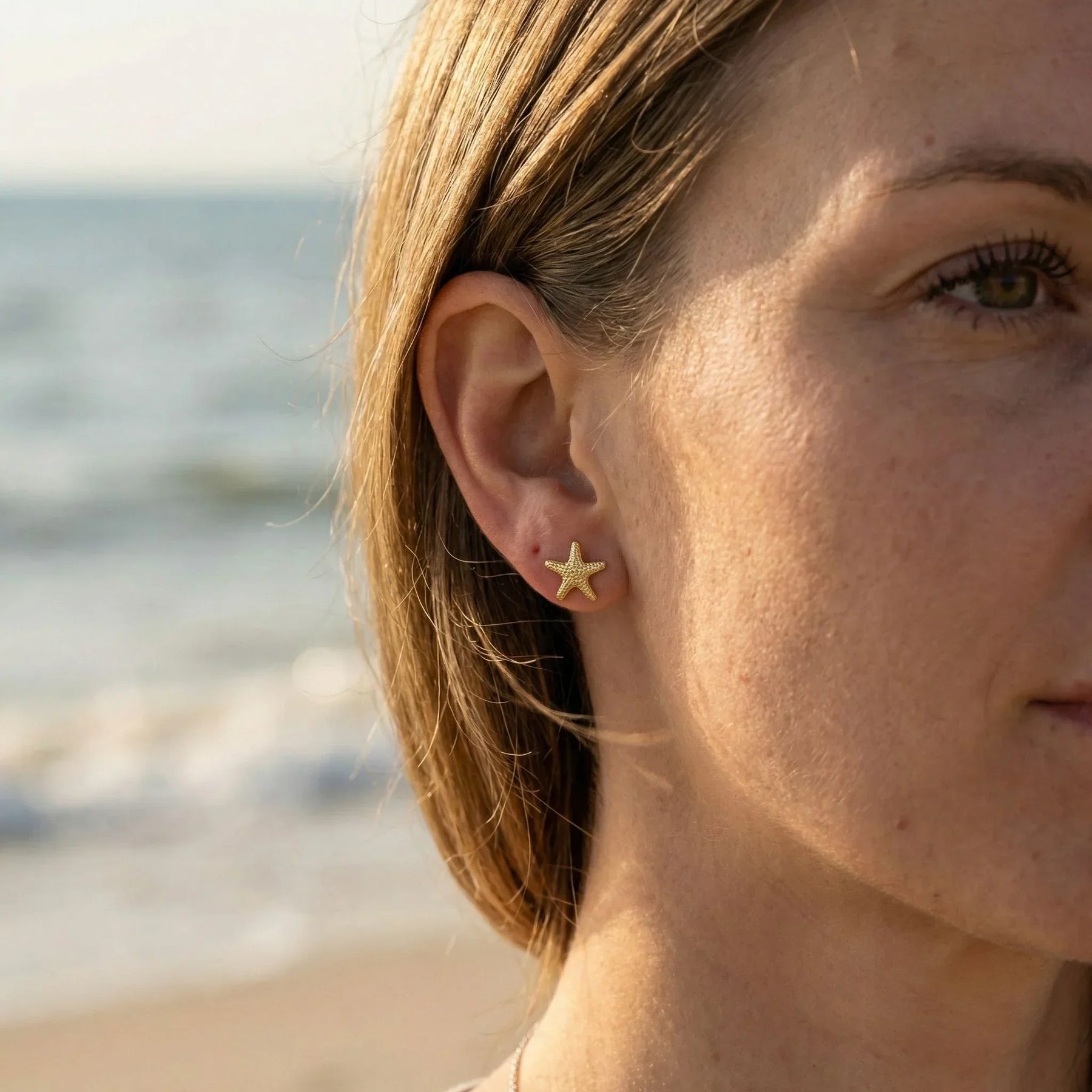 Goldener Seestern Ohrstecker am Ohr einer Frau am Strand, maritimer Schmuck