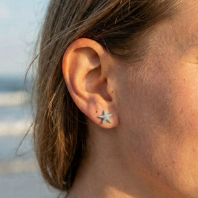 Silberner Seestern Ohrstecker am Ohr einer Frau, maritimer Schmuck, Strand im Hintergrund